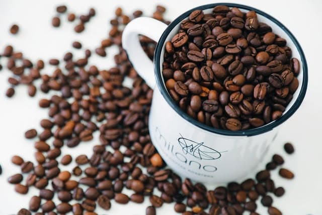 Roasted coffee beans spilling around a Milano-branded ceramic mug